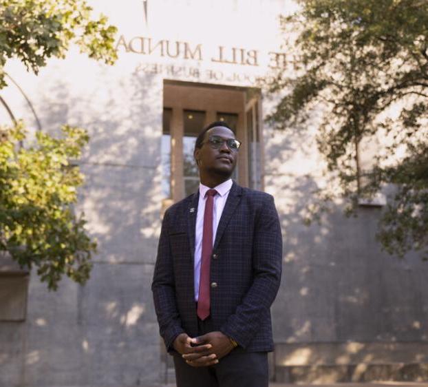 Emmanuel Epau wears a suit and stands outside of The Bill Munday School of Business.